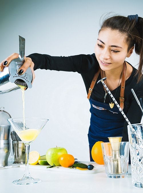 A mixologist straining a cocktail into a martini glass